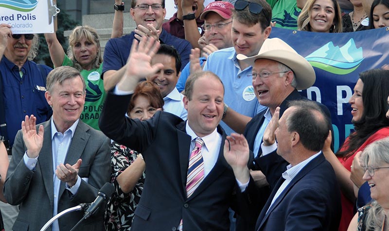 U.S. Rep. Jared Polis, center, Colorado's Democratic gubernatorial nominee, high-fives U.S. Rep. Ed Perlmutter as Gov. John Hickenlooper, state Rep. Alec Garnett, former Interior Secretary Ken Salazar and House Speaker Crisanta Duran applaud, at a rally on the steps of the state Capitol Friday, June 29, 2018, in Denver. (Photo by Ernest Luning/Colorado Politics)
